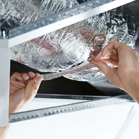 Hands securing a piece of reflective, foil-like insulation material inside a metal ceiling frame.