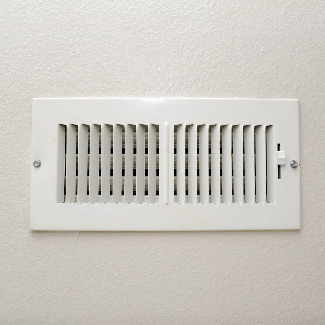 White wall air vent grille with horizontal slats and a small slider on the right