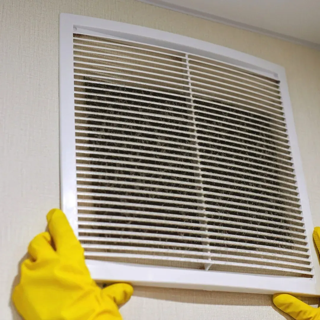 Gloved hands holding a dirty vent cover