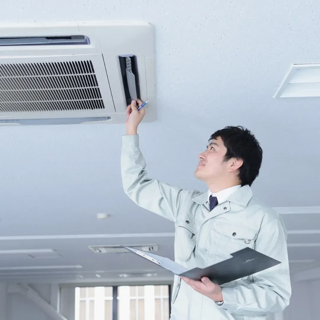Technician inspecting a ceiling vent with a clipboard in a bright room